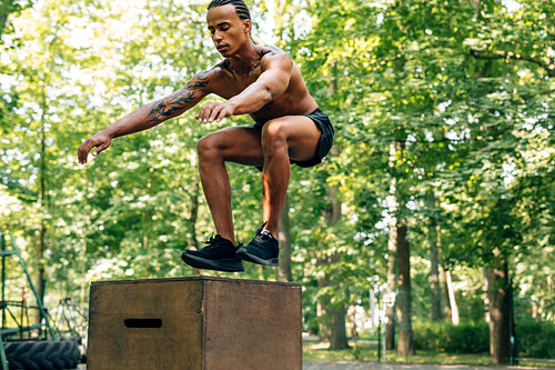 Young athletic male doing box jump on sports ground