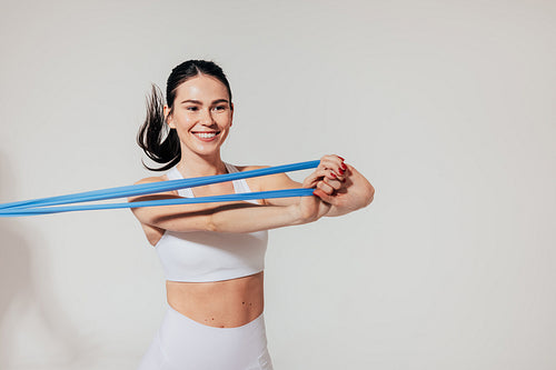 Happy sportswoman in white fitness wear pulling resistance band