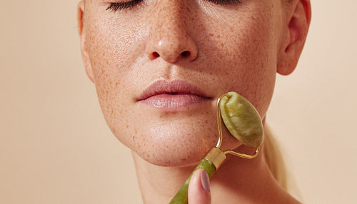 Close-up high detailed cropped shot of a young using a roller on her freckled skin