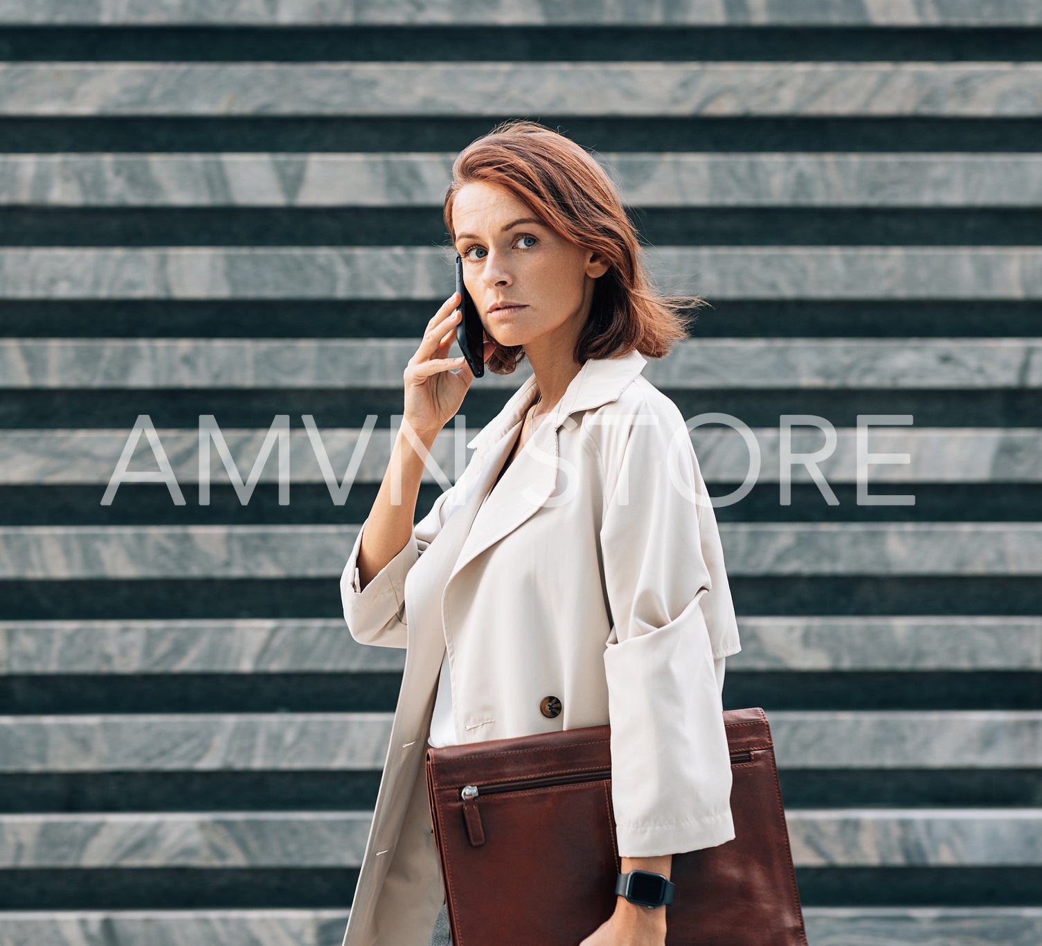 Confident businesswoman in coat talking on the mobile phone looking away