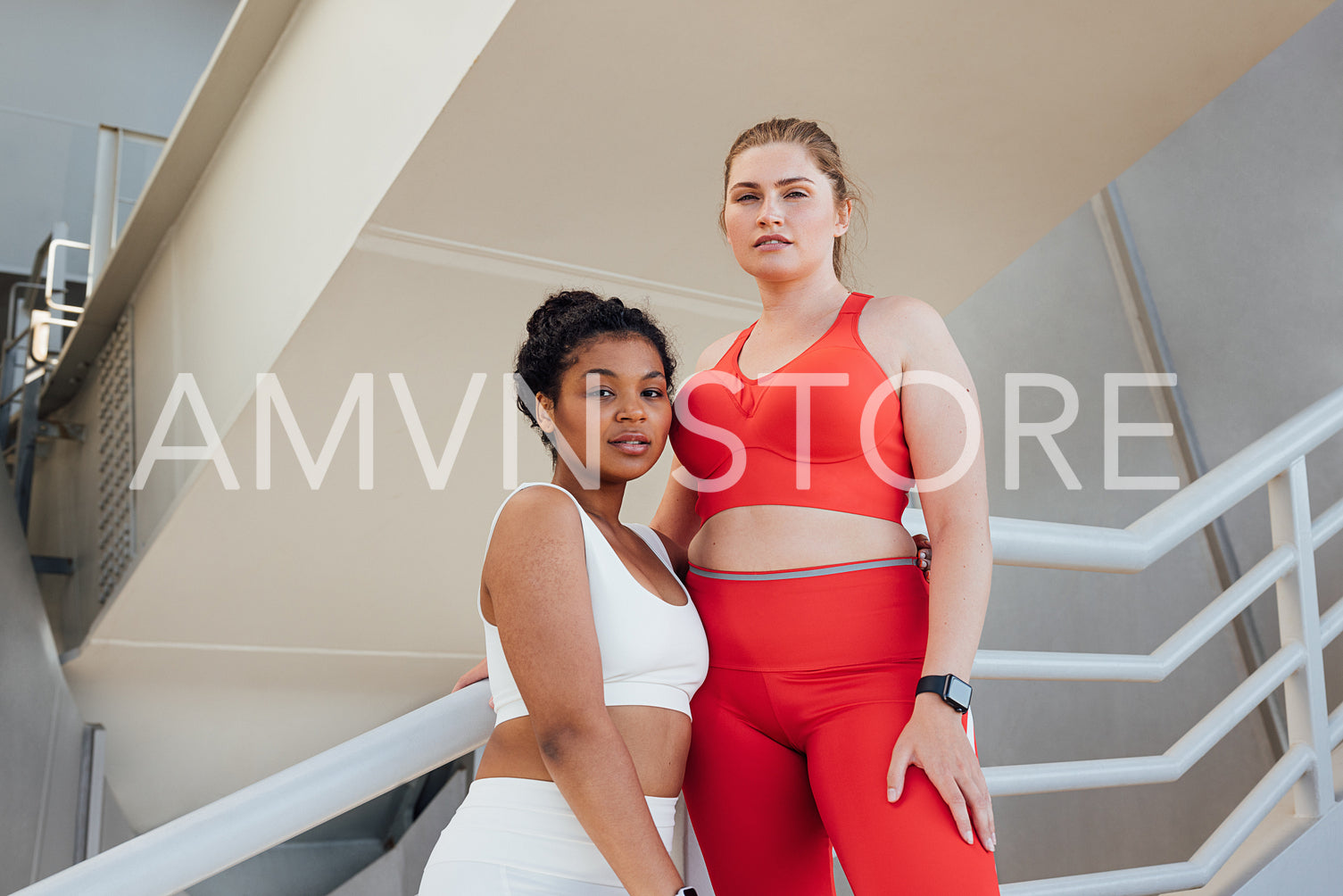 Portrait of two plus-size females in fitness attire looking at camera. Two plus-size athletes standing together outdoors relaxing after a workout.