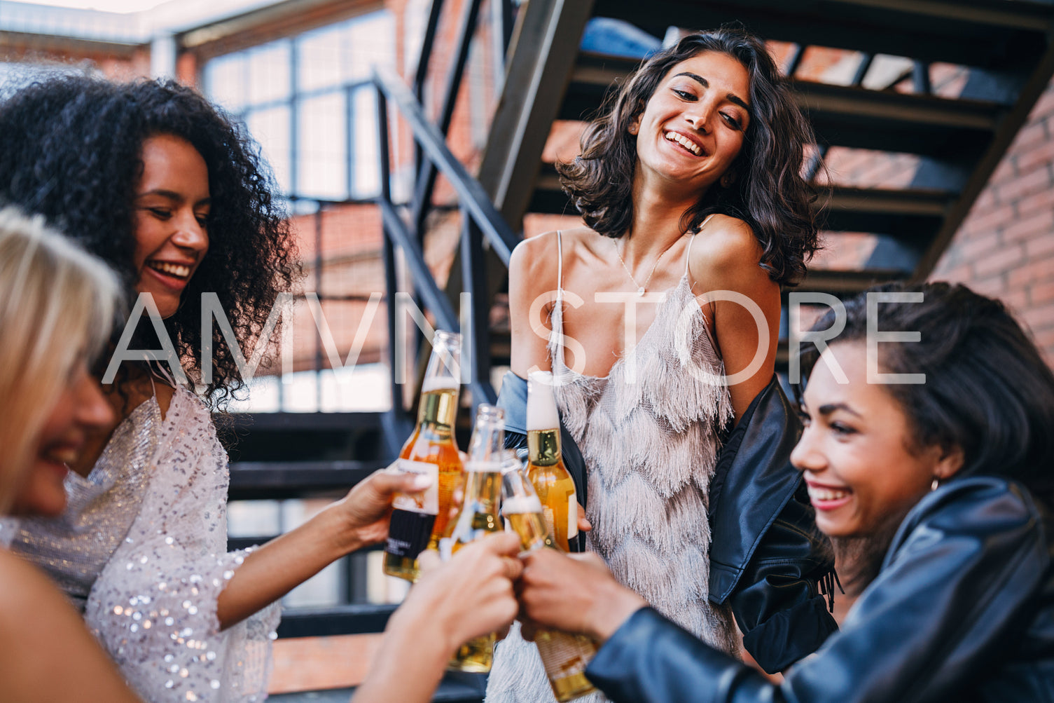 Beautiful laughing friends toasting with bottles of beer outdoors	