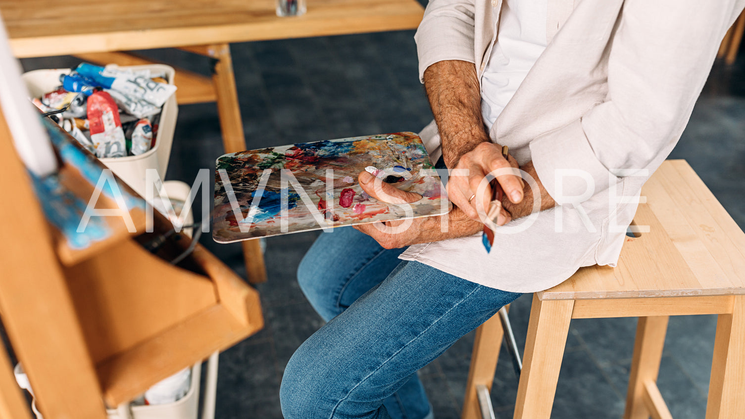 Unrecognizable male painter holding a palette and brush sitting on a chair	