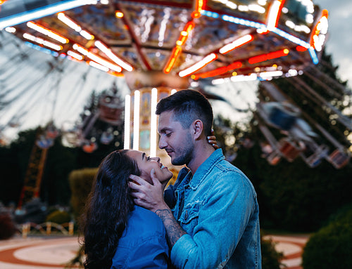 Happy couple in an amusement park. Young couple in love hugging and looking at each other against the carousel.