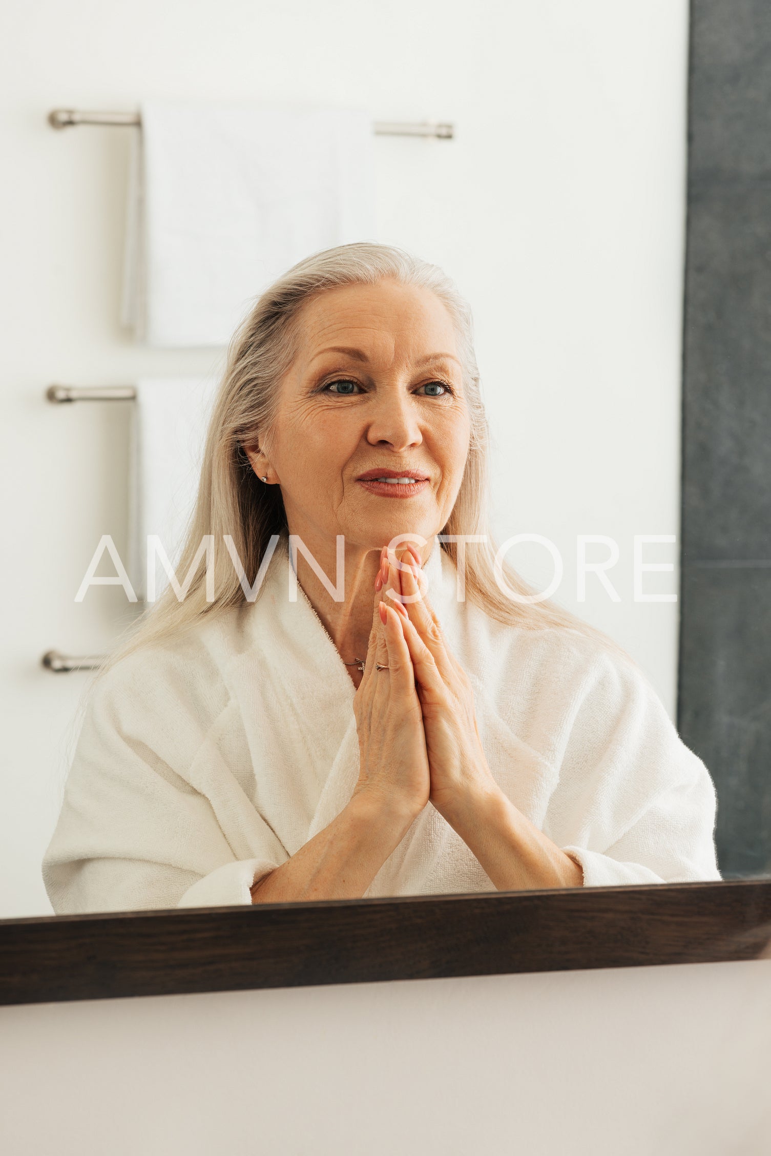 Senior woman in bathrobe admires her reflection in a bathroom mirror