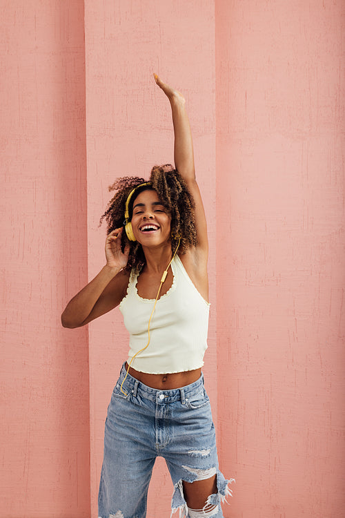 Young female having fun while listening to music against pink wa