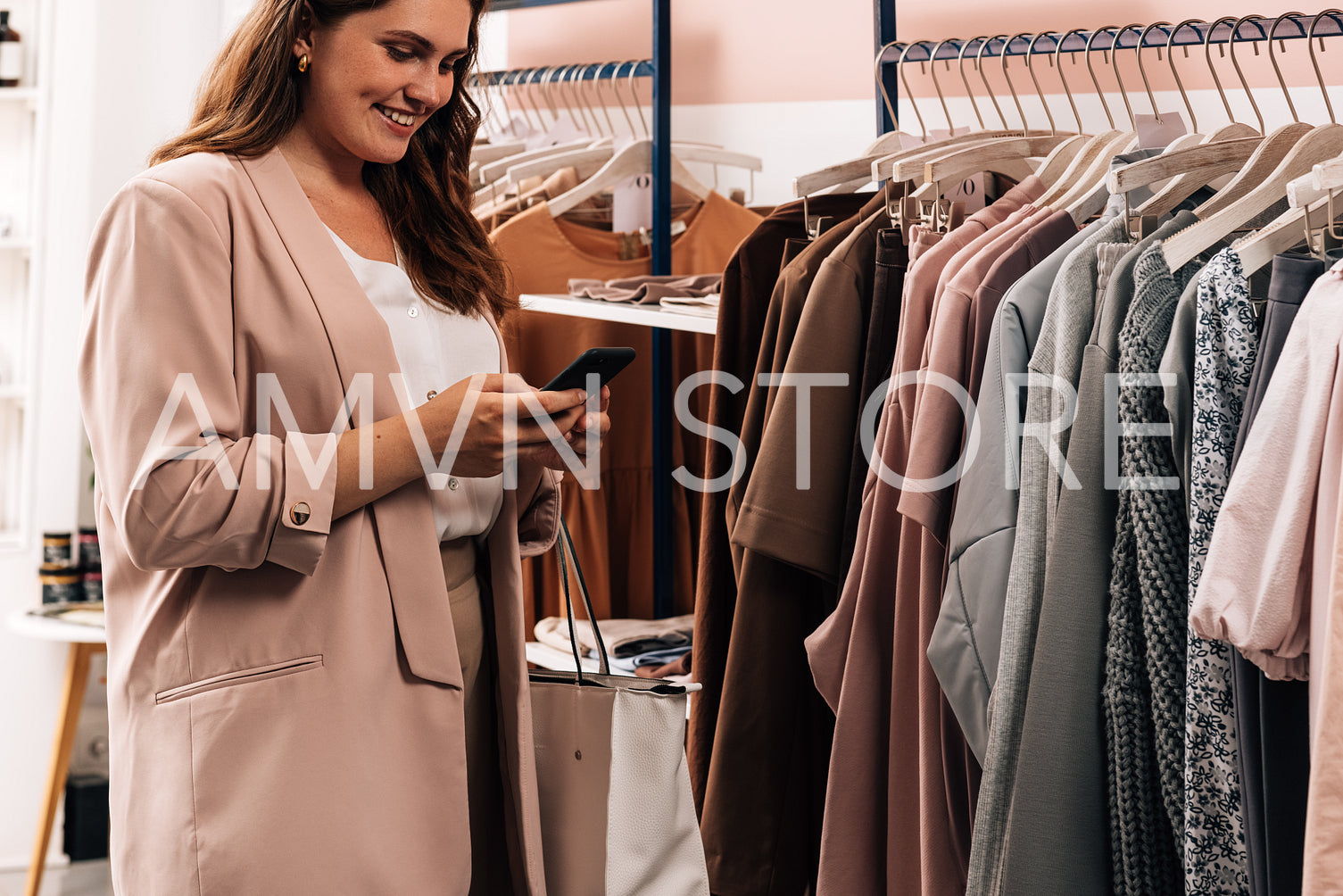 Smiling woman using cell phone while standing at a rack in a clo