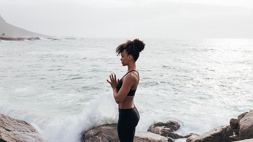 Side view of slim woman in sports clothes praying and meditating by ocean