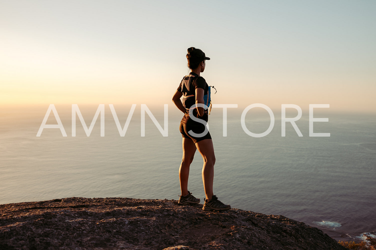 Woman hiker enjoying the view at sunset. Trail runner taking a break standing on the top of the mountain.