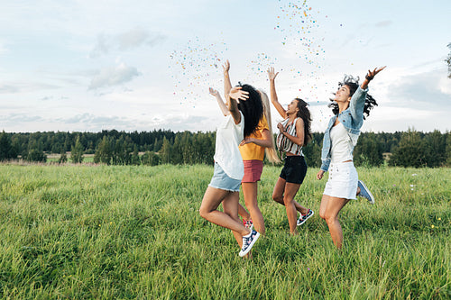 Side view of four female friends running on a field and throwing confetti