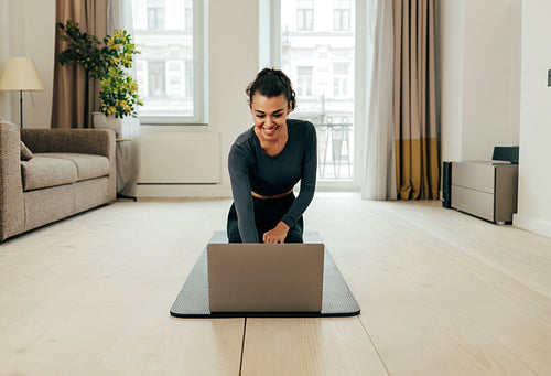 Woman in sportswear sitting on floor and using a laptop. Fitness female preparing for online sport class at home.