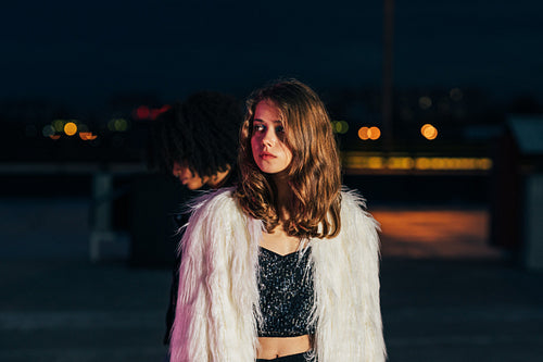 Young stylish woman looking away while standing on roof at night