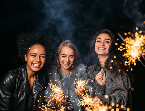 Three young women laughing at night and holding sparklers