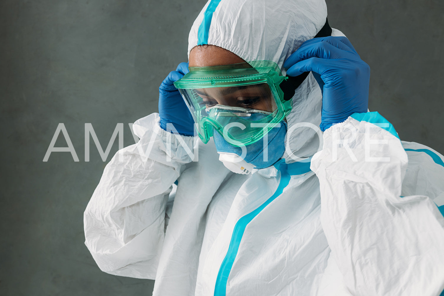 Female doctor adjusting protective glasses over a medical suit at wall	