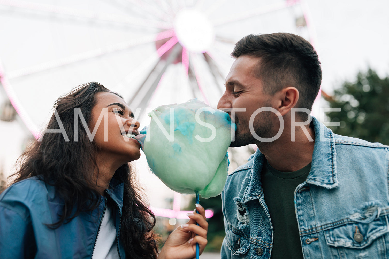 Young guys are having fun in an amusement park. Girlfriend and her boyfriend biting cotton candy during the festival.