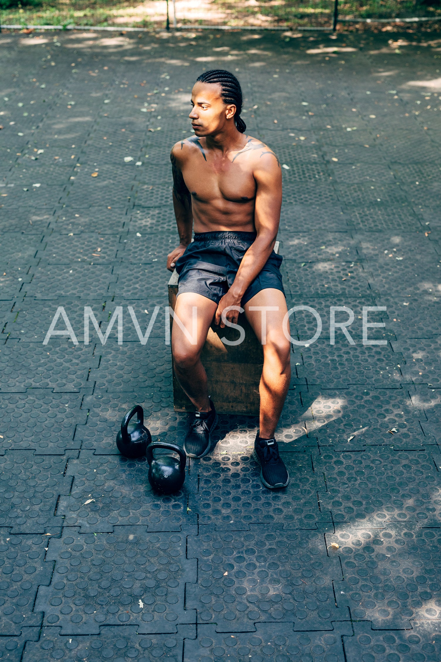 Bare-chested man sitting outdoors on jump box after training with kettlebells	