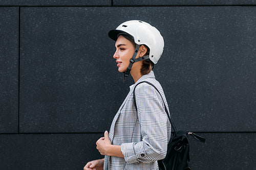 Side view of a good looking businesswoman in cycling helmet standing at black wall in the city