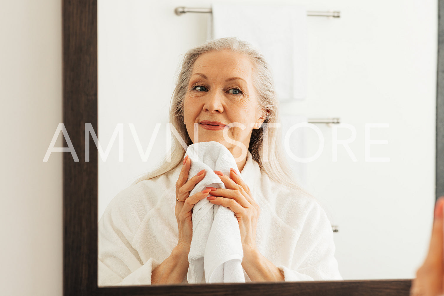 Senior woman with grey hair wiping her chin in front of a mirror