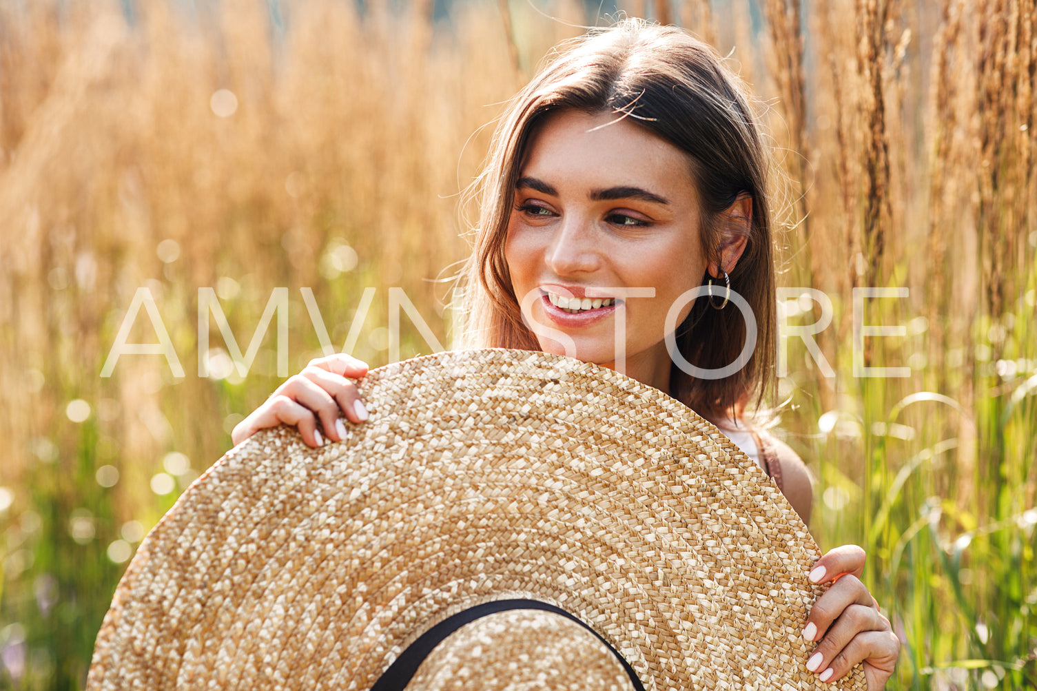 Smiling woman standing outdoors with big straw hat surrounded by tall grass	