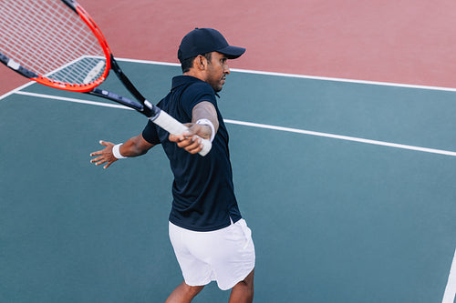 Professional tennis player practicing one-handed backhand hit on hard court