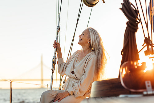 Side view of mature woman with long hair sitting on yacht and smiling