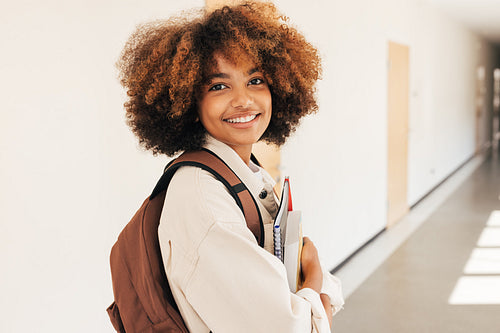Smiling girl standing in college corridor holding textbooks and looking at camera