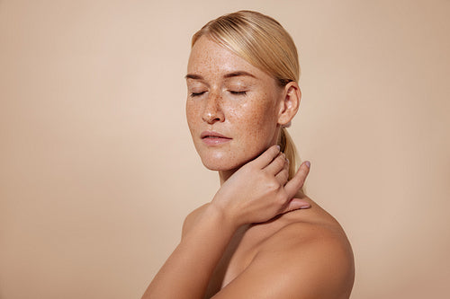 Caucasian female with freckles and blond hair standing with closed eyes massaging her neck