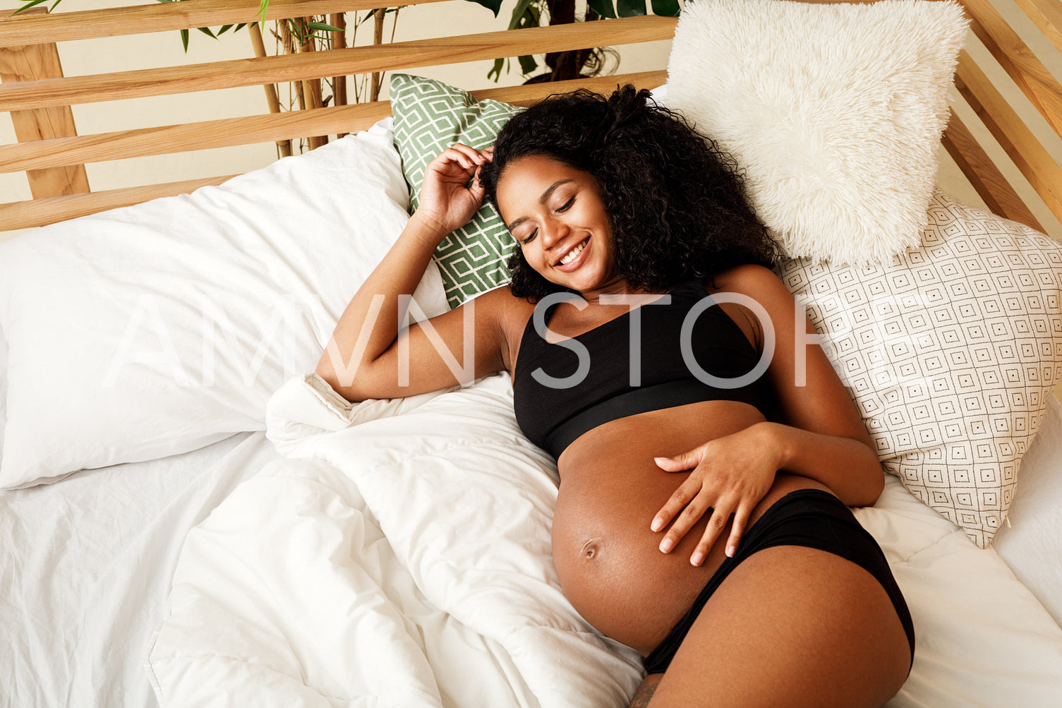 Smiling pregnant woman lying on bed at home, touching her belly	