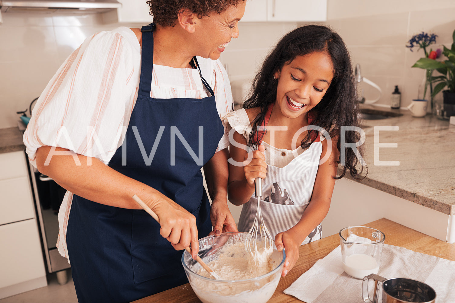 Happy girl and her grandma mixing dough in a glass bowl in a kitchen