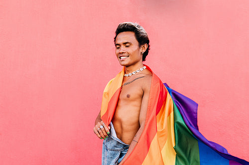 Happy guy with closed eyes holding a rainbow LGBT flag while sta