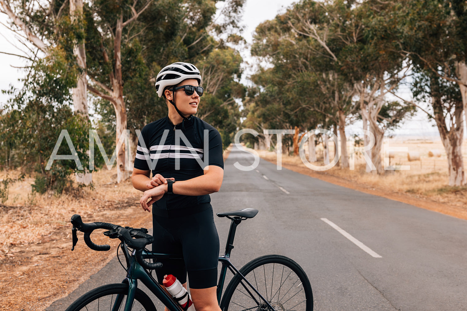 Woman cyclist with bicycle standing outdoors on countryside road and checking smartwatch