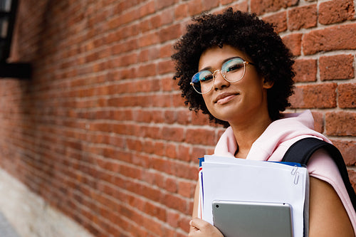 Teenage girl in glasses standing with books outdoors at wall