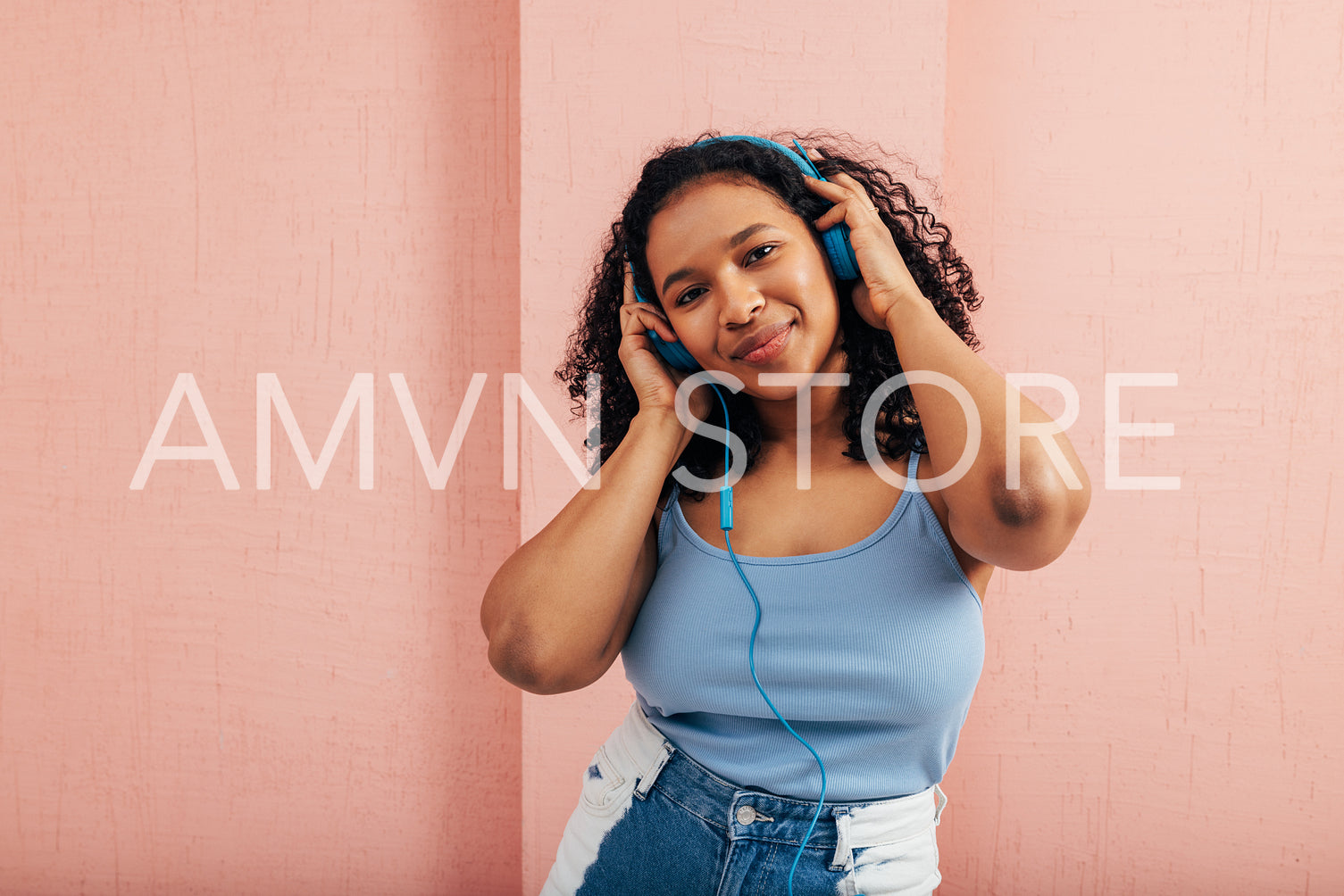 Plus size woman looking at camera wearing blue headphones against a pink wall