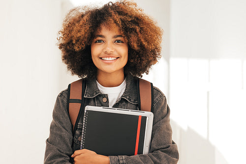 Close up portrait of a smiling student with textbook and laptop standing looking at camera