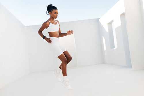 Full length of a slim female in white sportswear jumping outdoors. Professional fitness athlete doing warming up exercises.