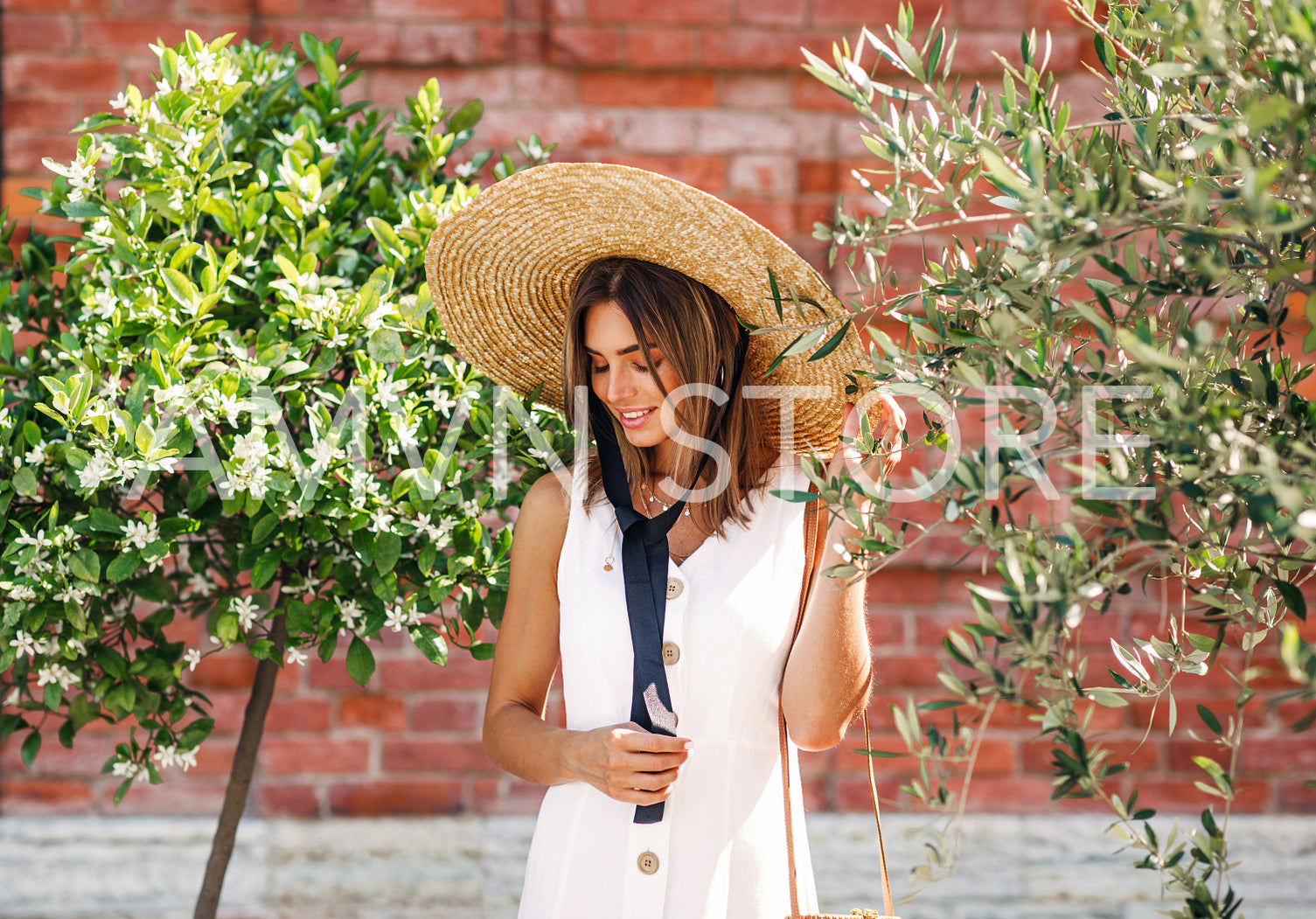 Stylish woman with straw hat standing between two trees and looking down	