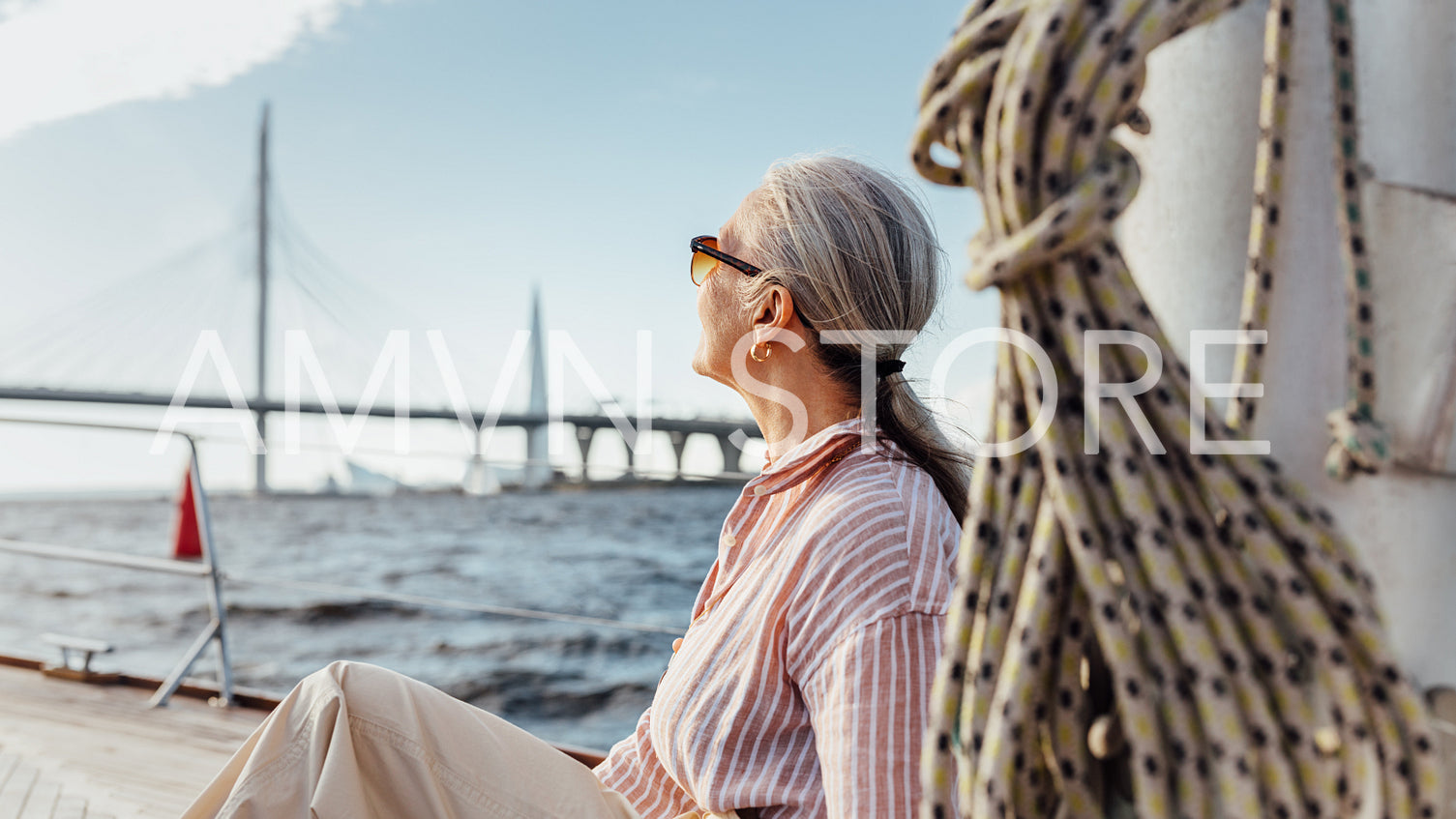 Senior woman with gray hair wearing sunglasses looking into the distance while sitting on a sailboat	