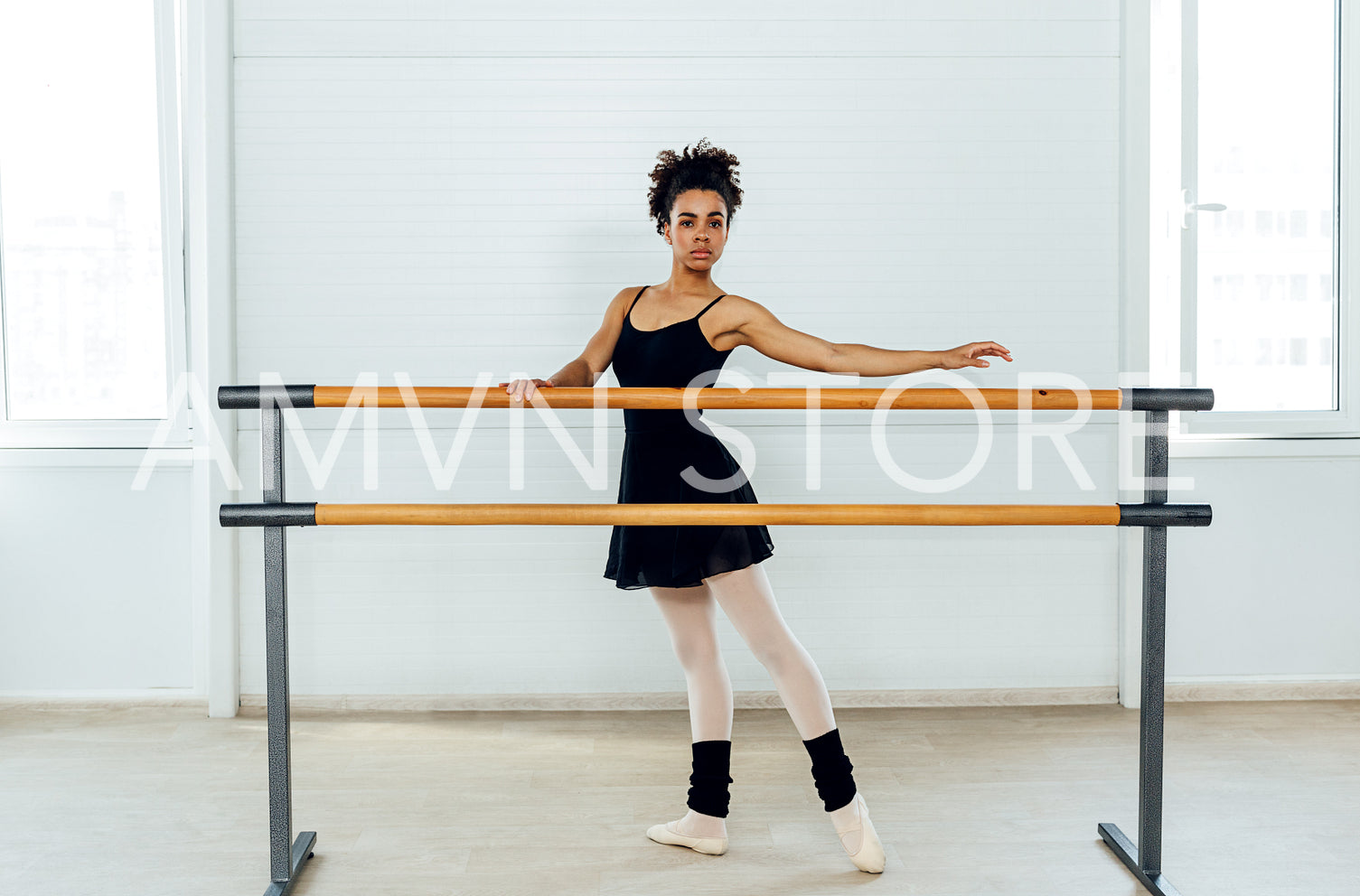 Female ballet dancer with curly hair holding a barre preparing for a ballet class in a studio	