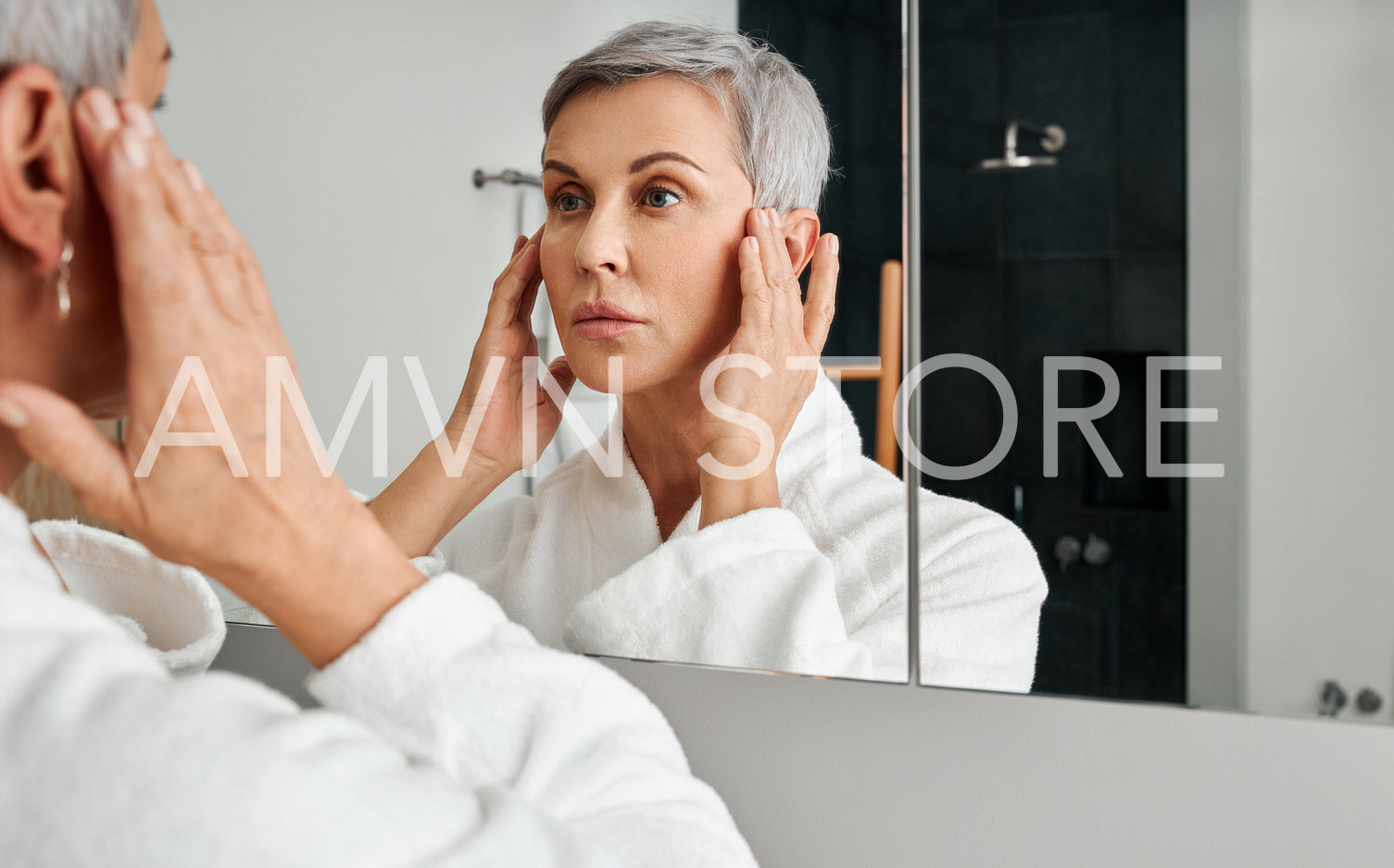 Mature woman in bathrobe looking herself in the bathroom mirror	