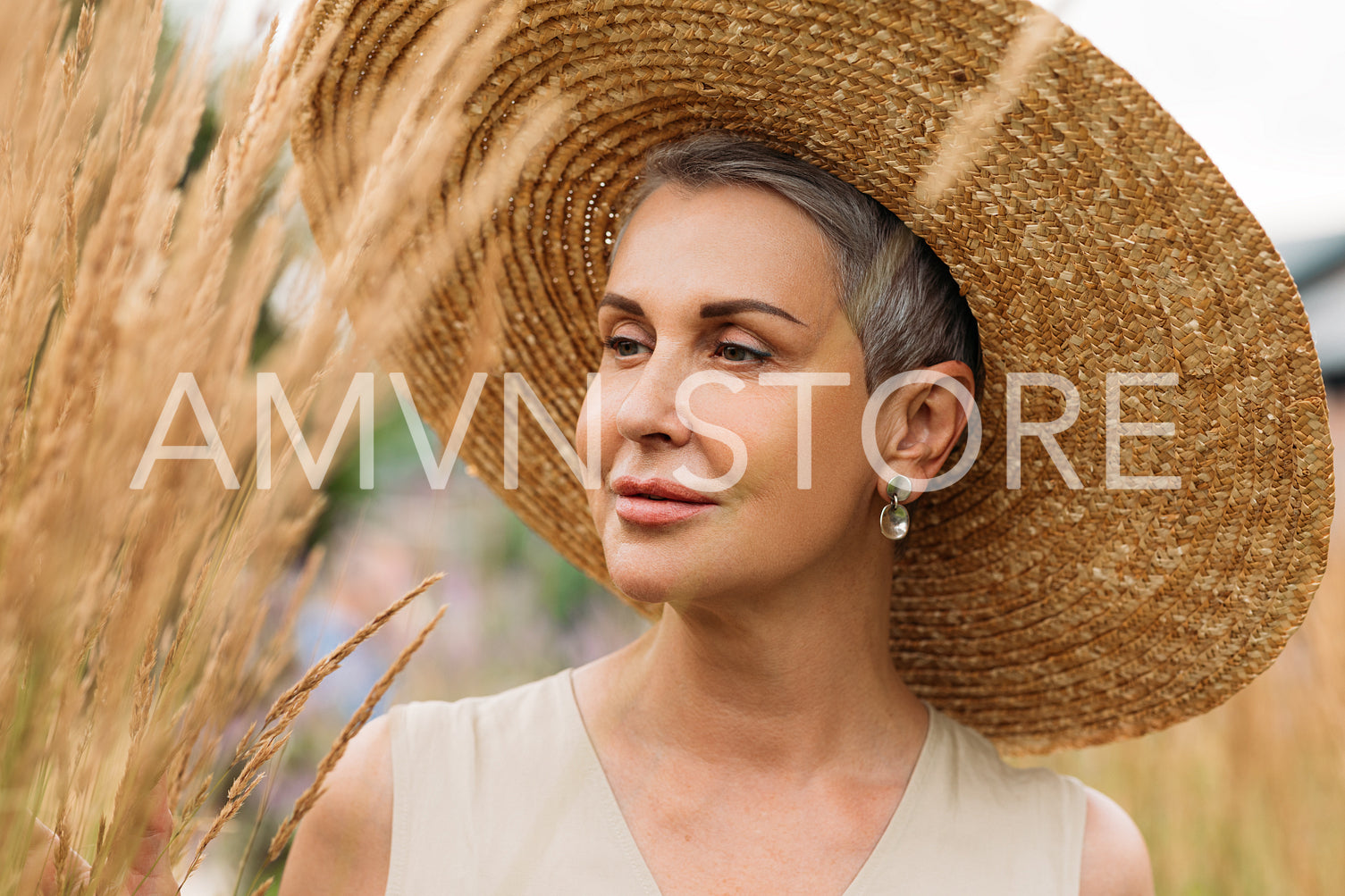 Aged female in a straw hat looking at wheat