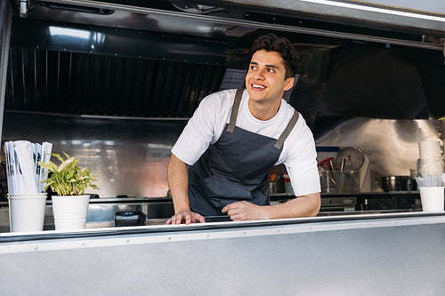 Portrait of a smiling food truck owner wearing apron leaning counter