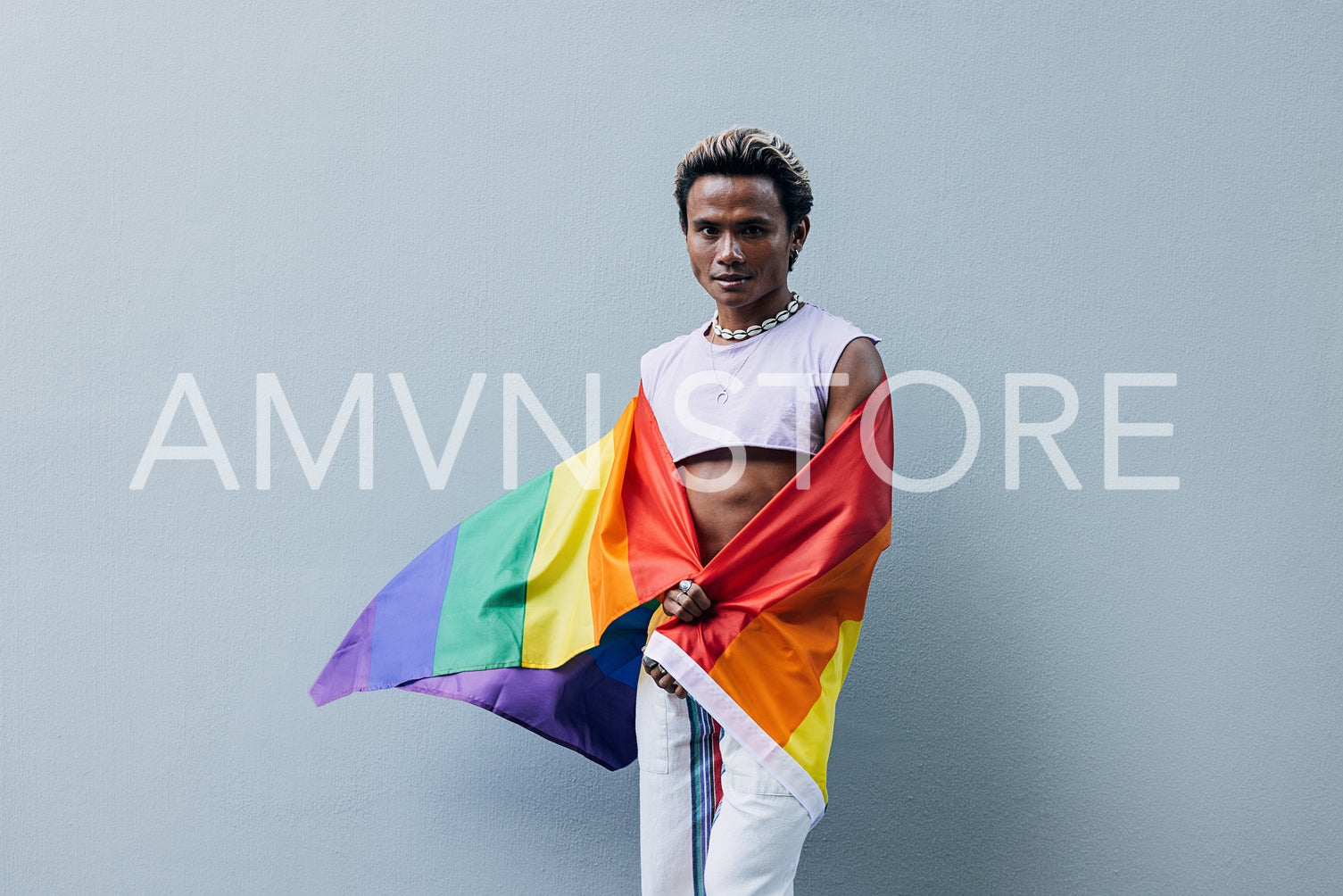 Man with a pride flag posing on grey background outdoors