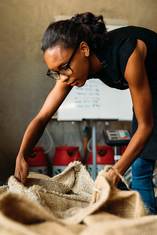 Woman at storage looking in a sack. Female worker choosing a coffee grade for roasting.