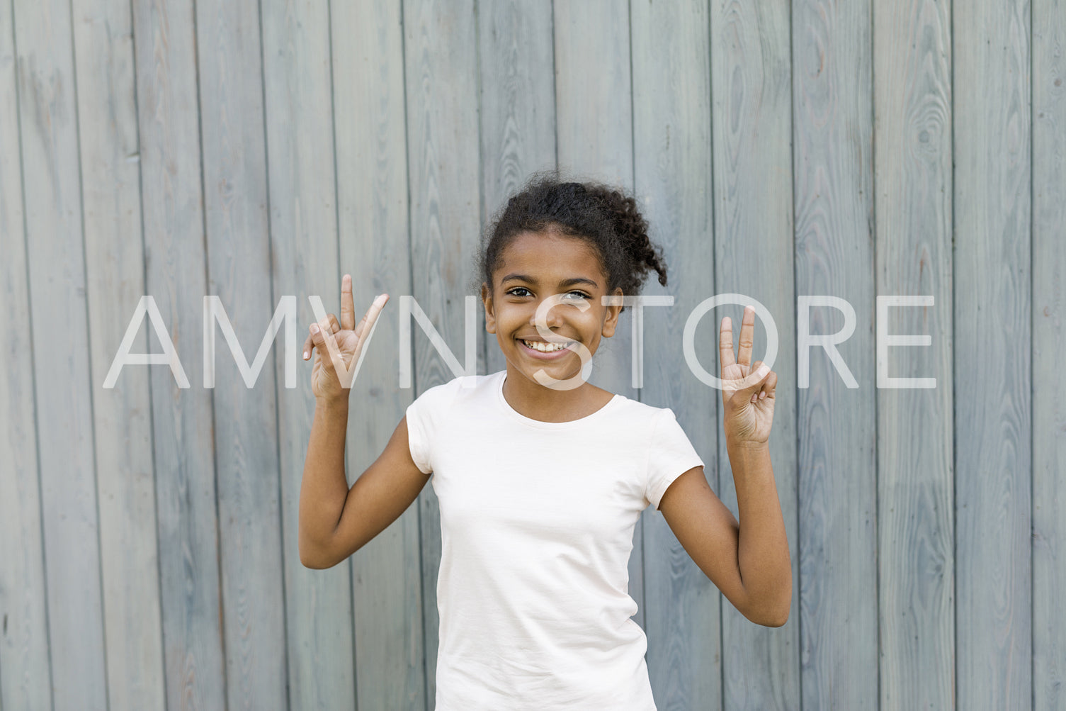 Happy girl standing at wall outdoors, making the victory sign with her hands	