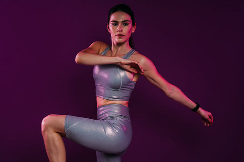 Woman in silver fitness attire doing warming-up exercises over a magenta backdrop