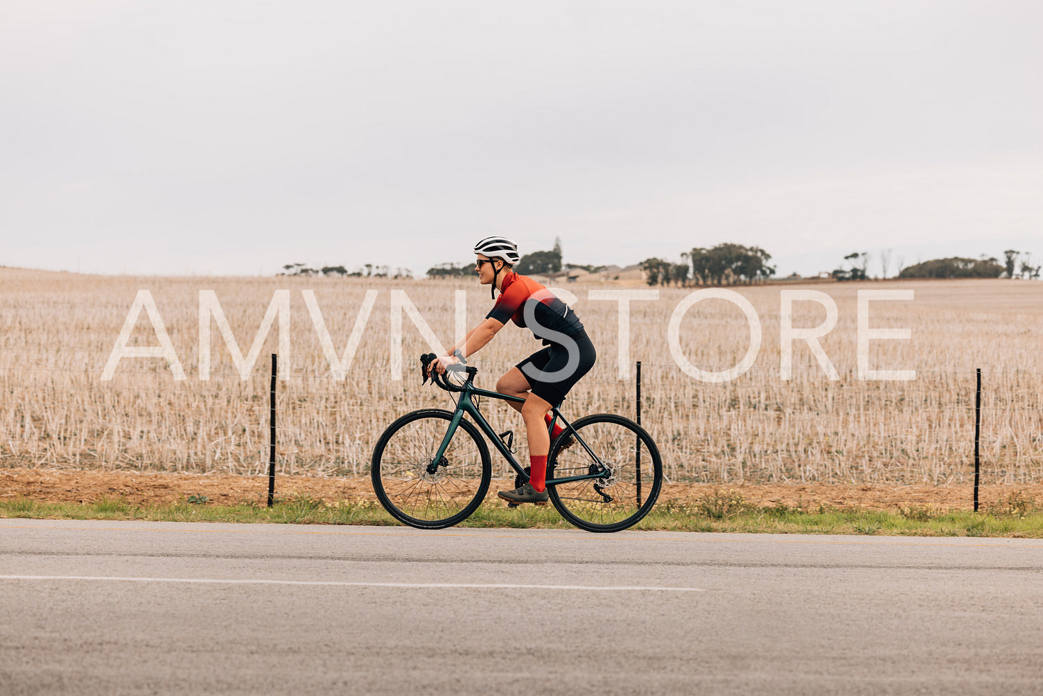 Side view of young woman cyclist in sportswear riding road bike against a field