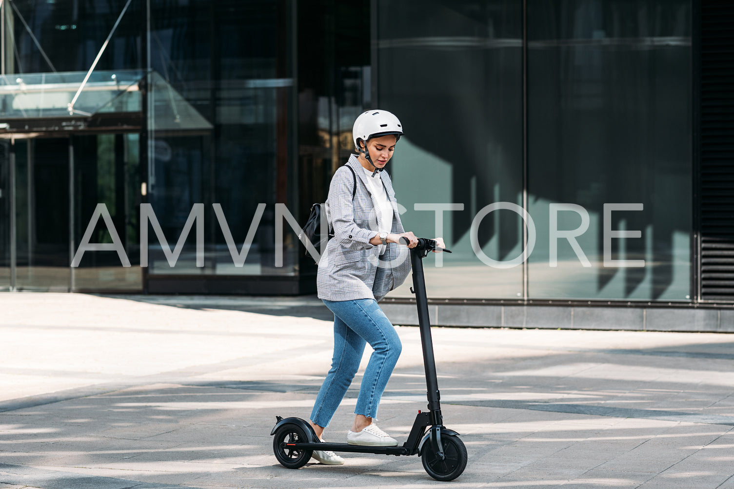 Young businesswoman with a safety helmet on her head driving electrical scooter near an office building