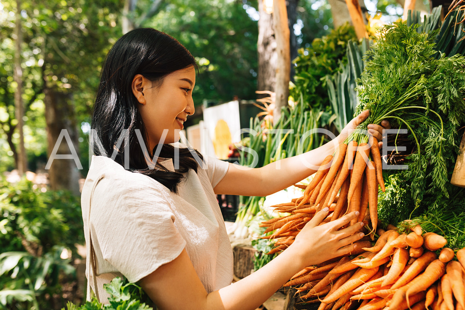 Smiling buyer holding a bunch of carrots. Asian woman choosing vegetables in the local market.