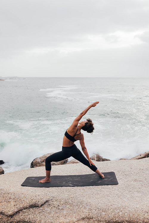 Female stretching her body while standing on a mat against ocean