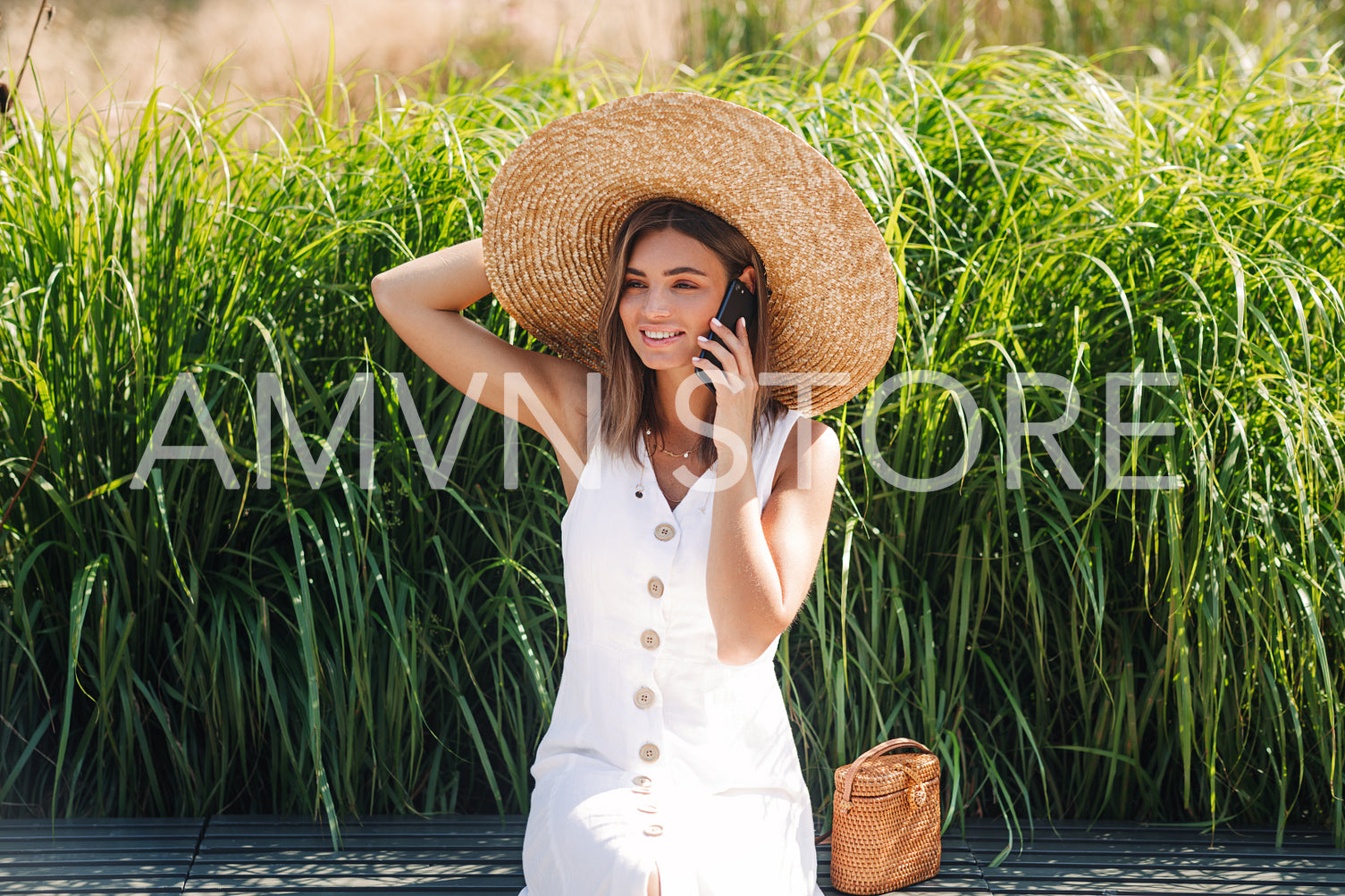 Smiling woman wearing big hat talking on cell phone in the park	